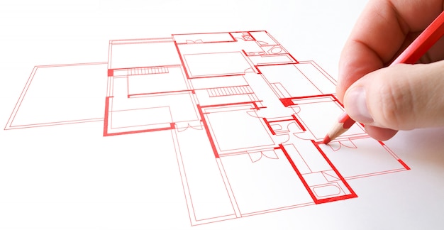 Una persona dibujando un plano de casa con papel de lápiz rojo.